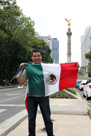 A dark-haired adult Mexican proudly raises the tricolor flag in Mexico City to celebrate his love for his country, culture and traditionsの写真素材