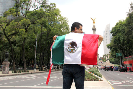A dark-haired adult Mexican proudly raises the tricolor flag in Mexico City to celebrate his love for his country, culture and traditionsの写真素材