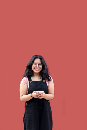 Brunette Latina teen woman with eyeglasses and brackets uses her cell phone to text, shop and date...