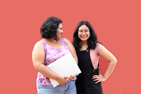 Two young 20 year old Latina brunette women use laptop and headphones for studying and entertainment watching music videosの写真素材