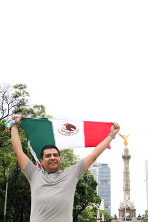 A dark-haired adult Mexican proudly raises the tricolor flag in Mexico City to celebrate his love for his country, culture and traditionsの写真素材