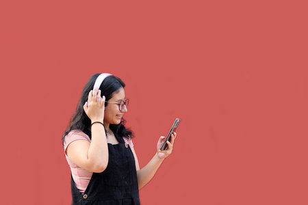Female Latina teenager of 17 years old uses her cell phone and audio to connect to music, podcast audiobooks and songs with her friendsの写真素材