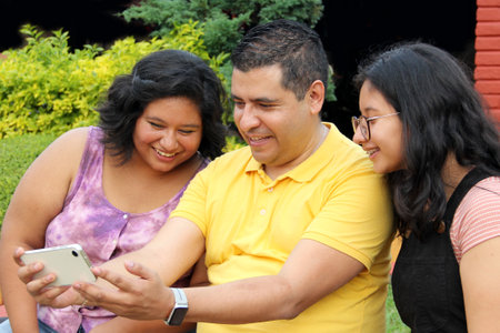 Divorced single dad with his dark-skinned Latino teenage daughters spending fun time using cell...