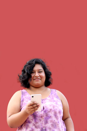 Young 20 year old Latina brunette woman uses her cell phone to send messages, make calls, buy, pay, study and make appointmentsの写真素材