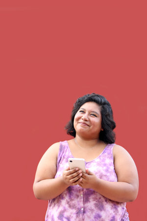 Young 20 year old Latina brunette woman uses her cell phone to send messages, make calls, buy, pay, study and make appointmentsの写真素材