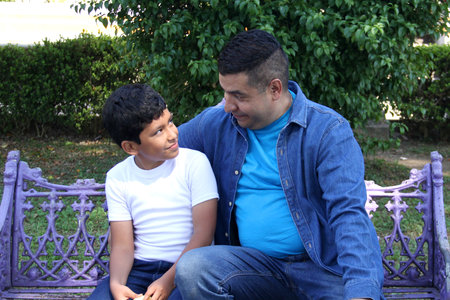 Divorced single dad on a park bench with his 10-year-old dark-skinned Latino son spending quality...