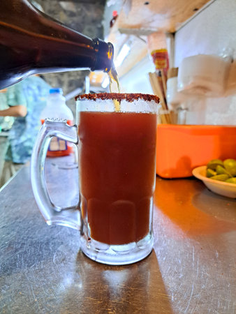 Hands preparing a michelada in a frosted jar with chili powder served with lemon, sauces and beer...