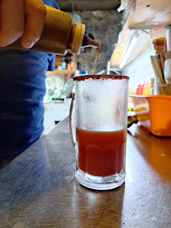 Hands preparing a michelada in a frosted jar with chili powder served with lemon, sauces and beer for a refreshing Mexican drinkの写真素材
