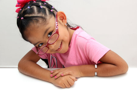 Brunette Latin girl with eye glasses, 4 years old, appears happy and calm at a school desk in...