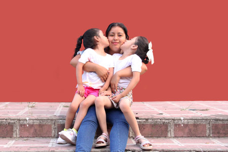 Young Latina mom hugs her two little daughters, they kiss each other and spend quality time...
