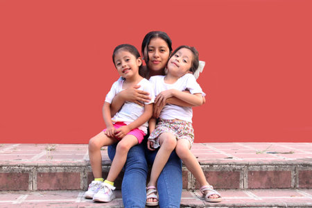 Young Latina mom hugs her two little daughters, they kiss each other and spend quality time...