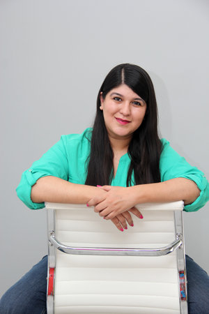 30-year-old Latin woman works sitting in an office chair and appears happy and satisfied with her...