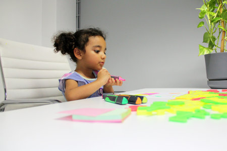 4 year old Latina girl with brunette curly hair draws as therapy with the school psychologist for...