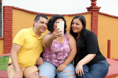 Family of dad, mom and young dark-skinned Latino daughter use their cell phone to make video calls, shop, take selfies and have a good time togetherの写真素材