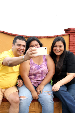 Family of dad, mom and young dark-skinned Latino daughter use their cell phone to make video calls,...