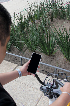 Dark-skinned Latino adult man uses his cell phone app to use a public bicycle for rent to improve...