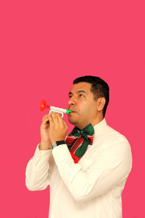Dark-skinned Latino adult man plays a toy tricolor trumpet with a bow with the colors of the Mexican...