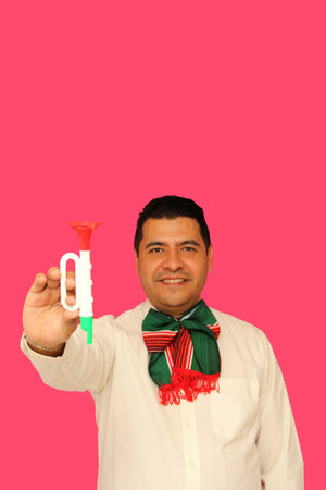 Mexican adult man with tricolor bow and toy trumpet celebrates the national holidays of Mexican...