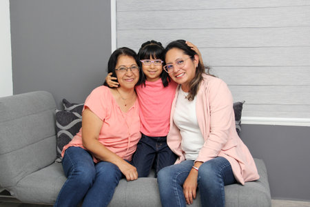 Three generations of brunette Latina women: grandmother, mom and daughter with glasses show their love and celebrate Mother's Dayの写真素材
