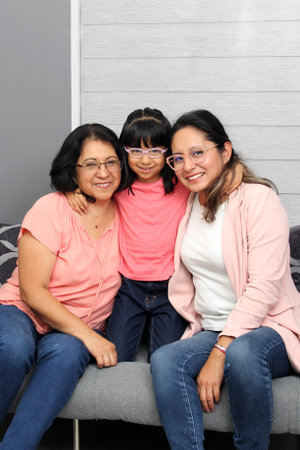 Three generations of brunette Latina women: grandmother, mom and daughter with glasses show their love and celebrate Mother's Dayの写真素材