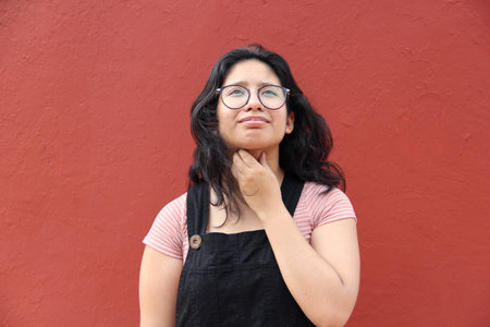 Young teenage woman with glasses Latin brunette suffers from cough and pain in throat due to...