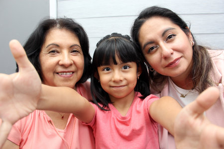 Three Generations of women Grandmother, mom and brunette Latina daughter with glasses show their...