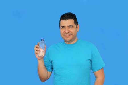 Dark-skinned Latino 40-year-old man shows a plastic bottle with plain water because hydration is...