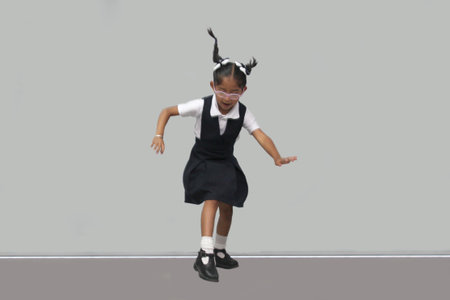 4 year old Latina brunette girl with glasses, braids and uniform jumps with happiness to celebrate...