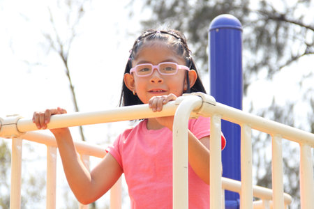 4 year old Latina brunette girl with glasses plays on the playground slide in the park enjoys the vacation weekendの写真素材