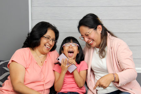 Latina brunette grandmother, mom and daughter use their cell phone to shop, watch movies, make video...