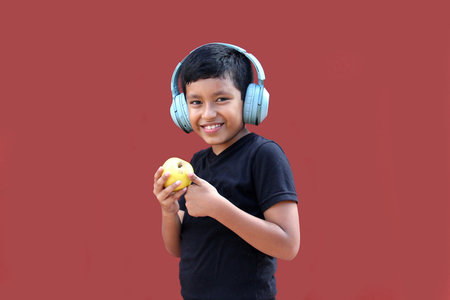 9-year-old dark-skinned Latino boy with headphones eats an apple as a sign of healthy eating while...