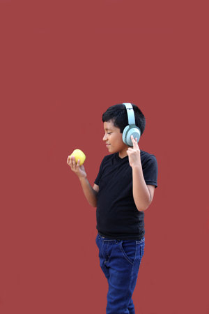 9-year-old dark-skinned Latino boy with headphones eats an apple as a sign of healthy eating while listening to musicの写真素材