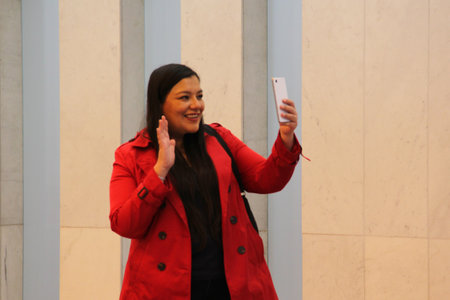 40-year-old Latina woman with long straight hair uses her cell phone in an office building, makes video calls, sends messages, takes selfies and makes purchasesの写真素材