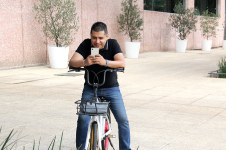 40-year-old dark-skinned Latino man uses an app on his cell phone to rent a public bicycle and...