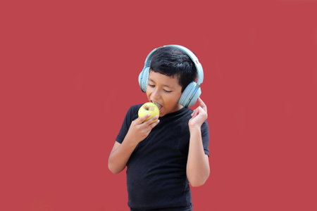 9-year-old dark-skinned Latino boy with noise-isolating headphones while eating an apple for healthy eatingの写真素材
