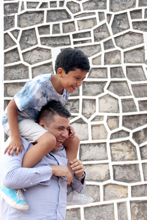 Divorced single dad carries his 9-year-old dark-skinned Latino son on his shoulders, plays and spends quality time together celebrating Father's Dayの写真素材