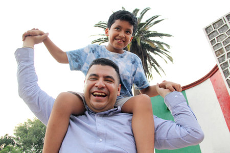 Divorced single dad carries his 9-year-old dark-skinned Latino son on his shoulders, plays and spends quality time together celebrating Father's Dayの写真素材