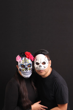 Couple of Mexican man and woman wear skull masks as costumes to celebrate the Day of the Dead in...