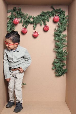 4 year old dark latino boy with glasses inside a cardboard gift box to celebrate Christmas and New...