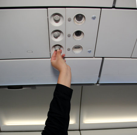 A person is interacting with an overhead panel in an airplane.の写真素材