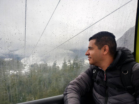 Latin adult man transports himself in gondola cabin to climb the snowy mountain to do sports and enjoy winterの写真素材