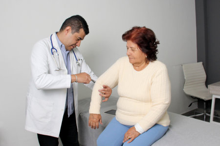 Dark-skinned Latino man medical doctor attends to elderly woman patient performs a reflex check in his officeの写真素材