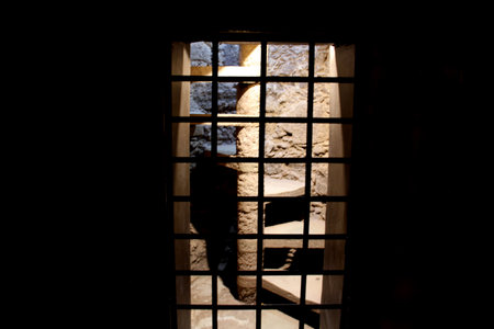 Old stone spiral stairs behind a grate in the dark and spooky basement of an old constructionの写真素材