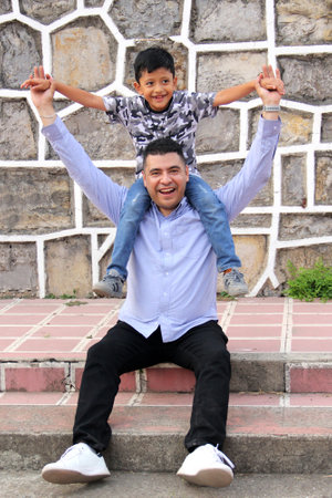 Single dad carries his 7 year old dark latin son like piggy back on his shoulders spending quality time celebrating Father's Dayの写真素材