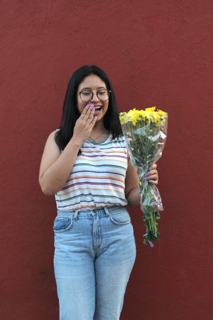 Young 17 year old brunette Latina teenager with glasses enthusiastically shows bouquet of yellow flowers to welcome love and springのeditorial素材