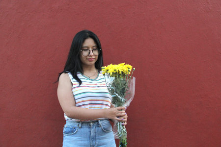 Young 17 year old brunette Latina teenager with glasses enthusiastically shows bouquet of yellow...