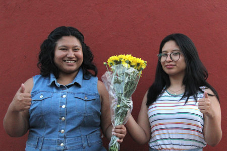 Young Latina sisters and friends, brunettes, give each other yellow flowers to show their love and...