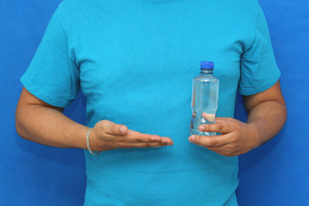 A dark-skinned man's hands hold and show a single-use plastic water bottle, a threat to the environment due to pollutionの写真素材