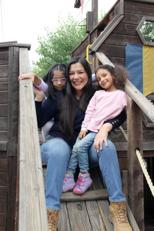 Single mother with two brunette Latina daughters play on playground equipment and spend time...