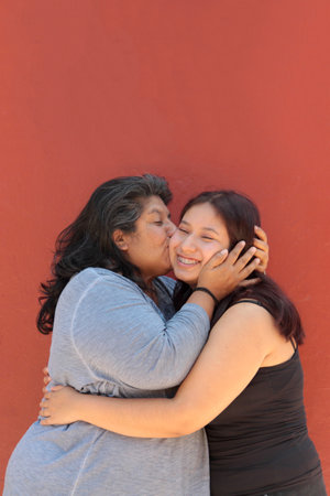 Divorced single mother and her 18-year-old Latina daughter show their love with kisses and hugs and celebrate Mother's Dayの写真素材
